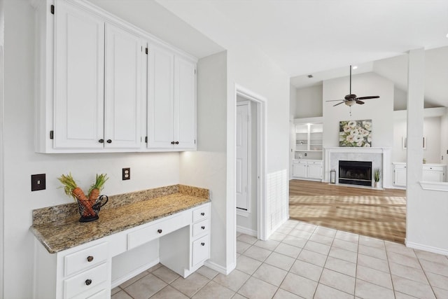 kitchen with built in desk, built in features, white cabinetry, dark stone countertops, and ceiling fan