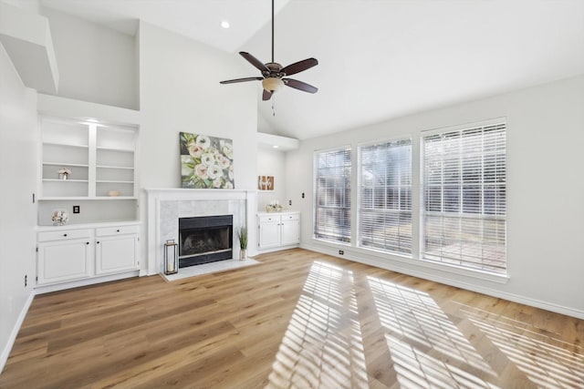 unfurnished living room with ceiling fan, a premium fireplace, high vaulted ceiling, and light wood-type flooring