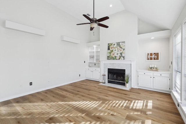 unfurnished living room featuring built in features, high vaulted ceiling, ceiling fan, a premium fireplace, and light wood-type flooring