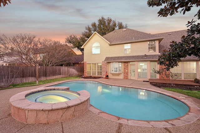 pool at dusk with a patio and an in ground hot tub