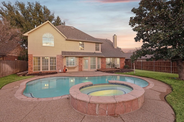 pool at dusk with an in ground hot tub, a yard, and a patio