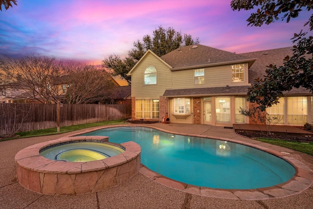 pool at dusk with an in ground hot tub and a patio