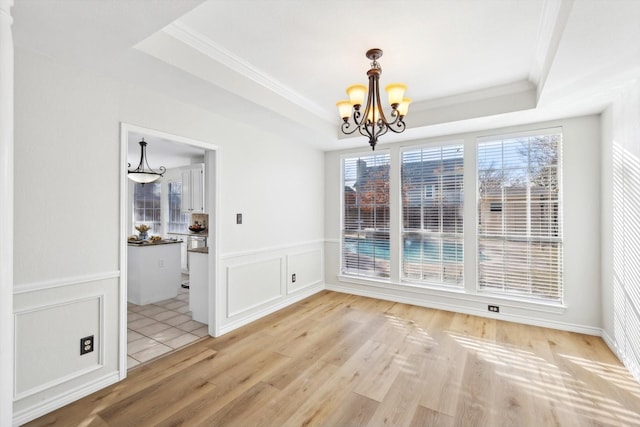 unfurnished dining area featuring an inviting chandelier, light hardwood / wood-style flooring, and a raised ceiling