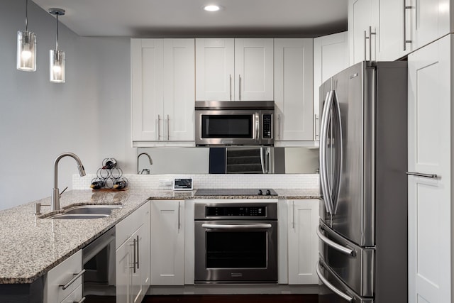 kitchen featuring light stone counters, decorative light fixtures, stainless steel appliances, white cabinetry, and a sink