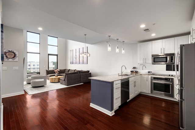 kitchen featuring visible vents, appliances with stainless steel finishes, a peninsula, light stone countertops, and a sink