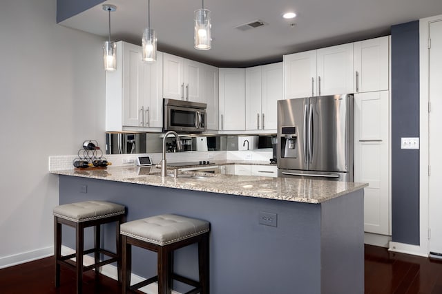 kitchen with a breakfast bar area, stainless steel appliances, a peninsula, visible vents, and light stone countertops