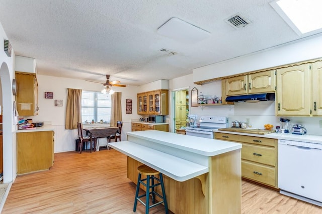 kitchen featuring white appliances, light hardwood / wood-style flooring, a breakfast bar, a textured ceiling, and a kitchen island