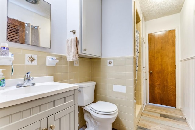 bathroom featuring hardwood / wood-style flooring, tile walls, vanity, a textured ceiling, and toilet