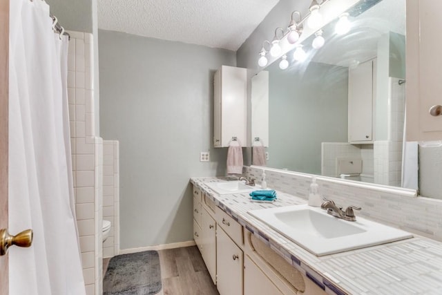 bathroom featuring toilet, a textured ceiling, vanity, hardwood / wood-style floors, and backsplash