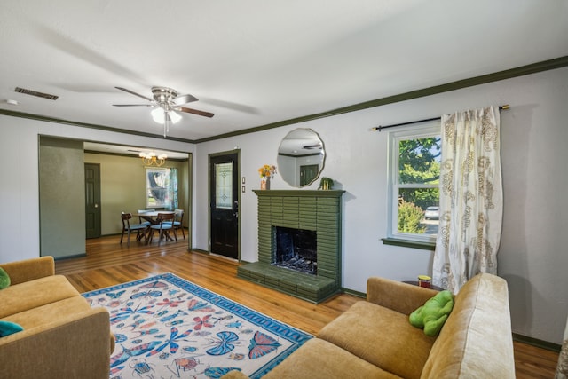 living room featuring wood-type flooring, a chandelier, a fireplace, and crown molding