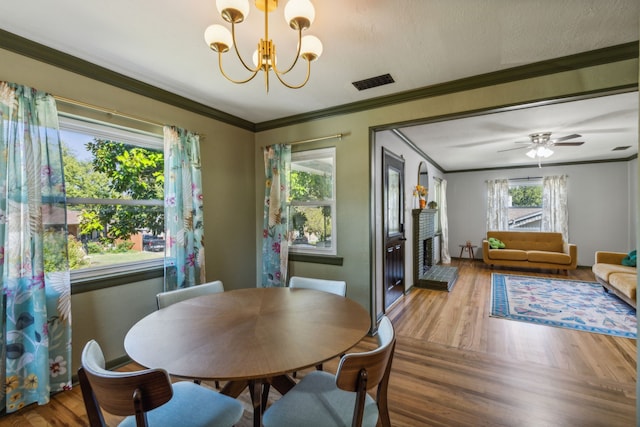 dining area with a fireplace, hardwood / wood-style flooring, ceiling fan with notable chandelier, and ornamental molding