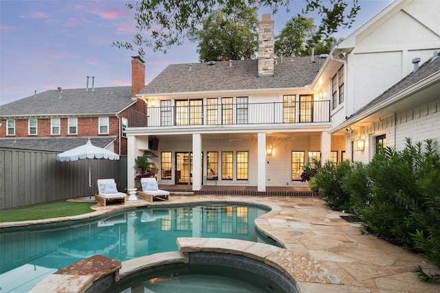 back house at dusk featuring a patio, a balcony, and a pool with hot tub