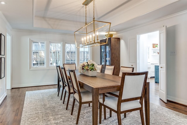 dining room with dark wood-type flooring, ornamental molding, a tray ceiling, and an inviting chandelier