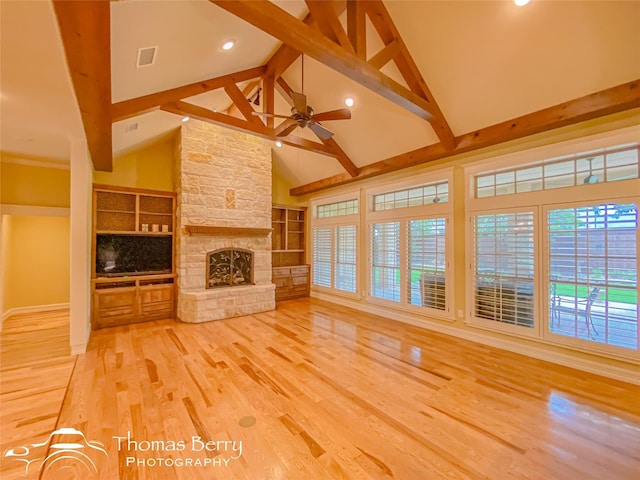 unfurnished living room featuring a stone fireplace, high vaulted ceiling, ceiling fan, beam ceiling, and hardwood / wood-style floors