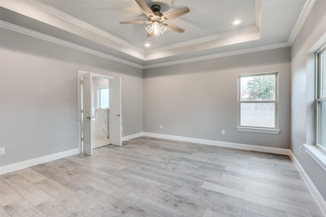 empty room with crown molding, a tray ceiling, ceiling fan, and light wood-type flooring