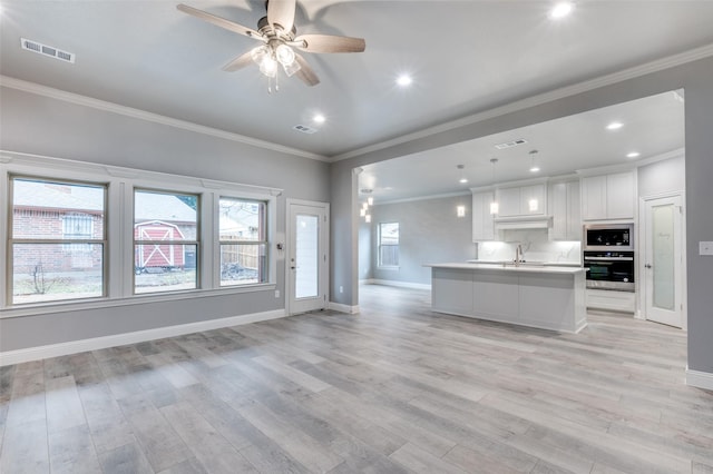 kitchen featuring sink, white cabinets, a center island with sink, decorative light fixtures, and stainless steel oven