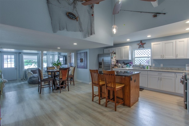 kitchen featuring stainless steel fridge with ice dispenser, light wood-type flooring, a kitchen breakfast bar, a kitchen island, and white cabinets