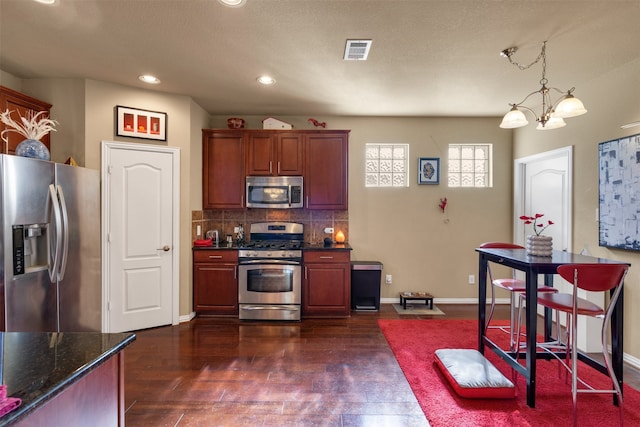 kitchen with an inviting chandelier, hanging light fixtures, dark stone counters, stainless steel appliances, and decorative backsplash