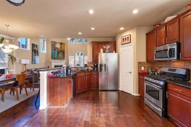 kitchen featuring dark wood-type flooring, appliances with stainless steel finishes, decorative light fixtures, and tasteful backsplash