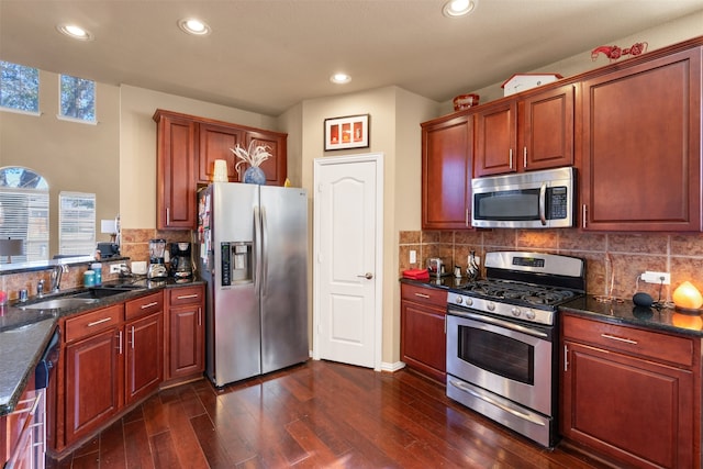 kitchen with sink, tasteful backsplash, dark stone countertops, appliances with stainless steel finishes, and dark hardwood / wood-style floors