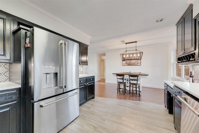 kitchen with stainless steel appliances, decorative light fixtures, decorative backsplash, and light wood-type flooring