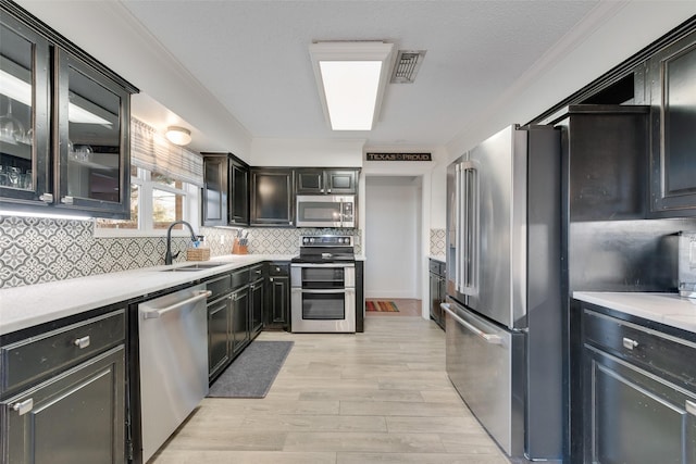 kitchen with sink, light hardwood / wood-style flooring, ornamental molding, appliances with stainless steel finishes, and decorative backsplash