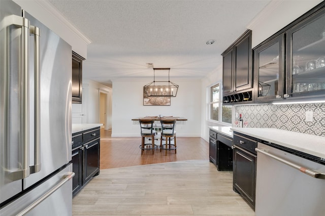 kitchen with appliances with stainless steel finishes, pendant lighting, tasteful backsplash, crown molding, and light hardwood / wood-style flooring