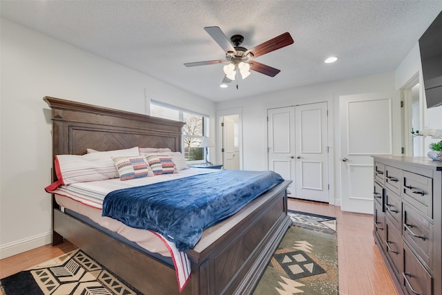 bedroom featuring ceiling fan, light hardwood / wood-style floors, a closet, and a textured ceiling