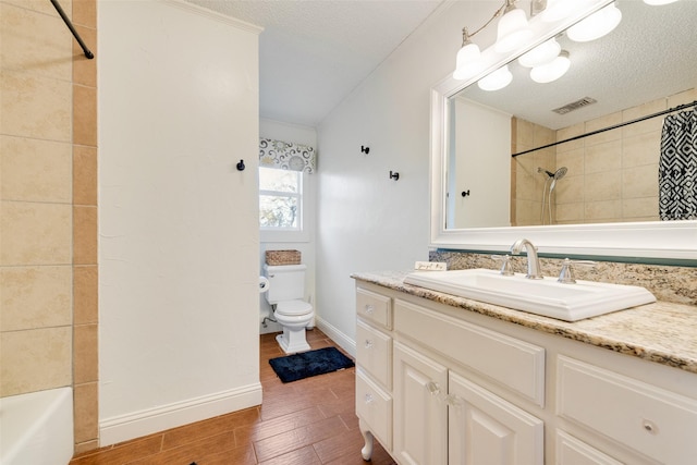 full bathroom with hardwood / wood-style flooring, vanity, tiled shower / bath combo, toilet, and a textured ceiling