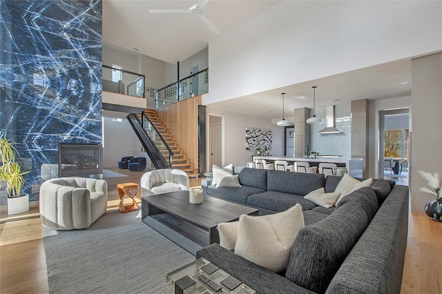 living room with hardwood / wood-style flooring, ceiling fan, a towering ceiling, and a high end fireplace