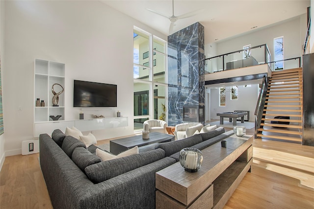 living room with ceiling fan, a fireplace, hardwood / wood-style floors, and a high ceiling