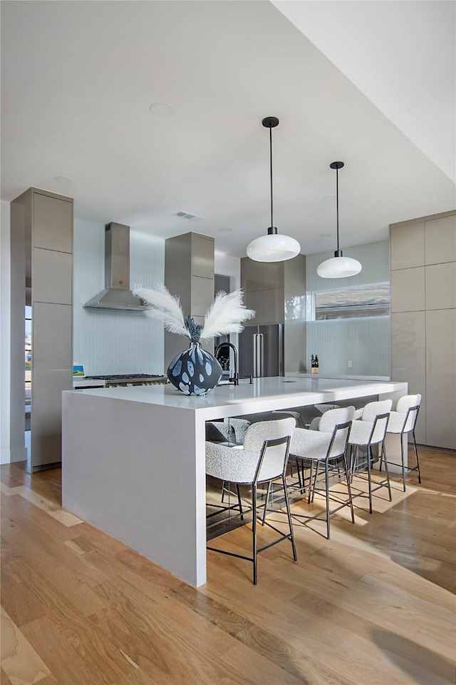 kitchen with light hardwood / wood-style flooring, gray cabinetry, a kitchen bar, and wall chimney exhaust hood