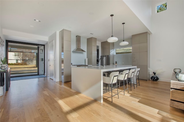 kitchen with wall chimney range hood, sink, light hardwood / wood-style flooring, a breakfast bar, and gray cabinetry