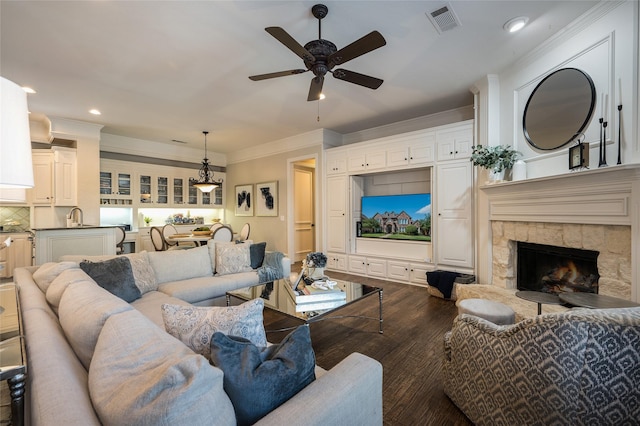 living room with ornamental molding, a stone fireplace, sink, and hardwood / wood-style floors