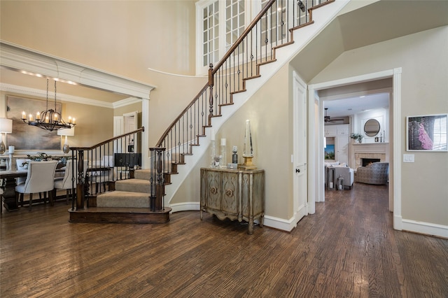 staircase featuring a tile fireplace, ceiling fan with notable chandelier, hardwood / wood-style flooring, a high ceiling, and crown molding