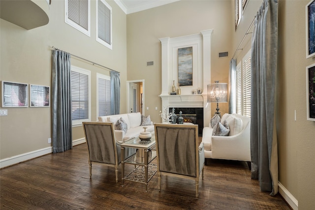 living area with dark wood-type flooring, a towering ceiling, a fireplace, and crown molding