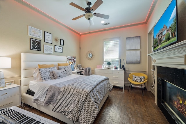 bedroom featuring ceiling fan, ornamental molding, a premium fireplace, and dark hardwood / wood-style flooring