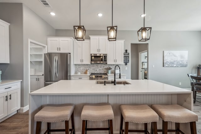 kitchen with appliances with stainless steel finishes, sink, a center island with sink, and decorative light fixtures