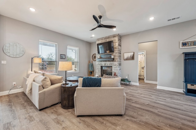 living room featuring ceiling fan, a fireplace, and light hardwood / wood-style flooring