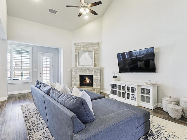 living room with dark hardwood / wood-style flooring, a stone fireplace, high vaulted ceiling, and ceiling fan