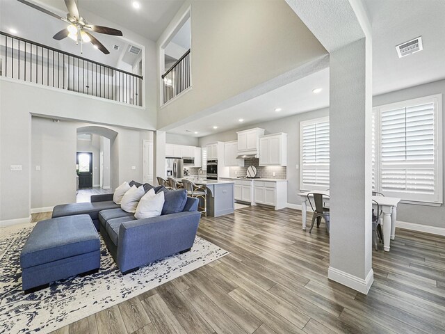 living room with a stone fireplace, dark wood-type flooring, sink, and ceiling fan