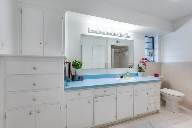 bathroom with a shower, tile walls, vanity, toilet, and tile patterned floors