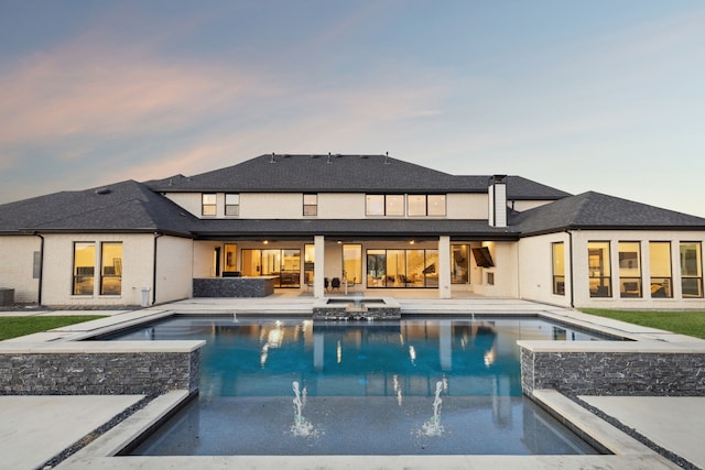 pool at dusk featuring an in ground hot tub, pool water feature, and a patio area