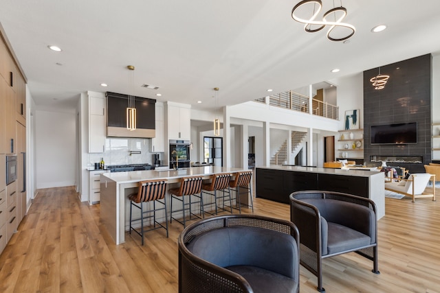 kitchen featuring a kitchen bar, hanging light fixtures, an island with sink, oven, and white cabinets