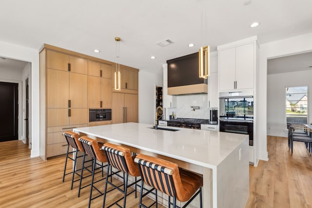 kitchen with pendant lighting, a breakfast bar, a kitchen island with sink, white cabinetry, and stainless steel double oven