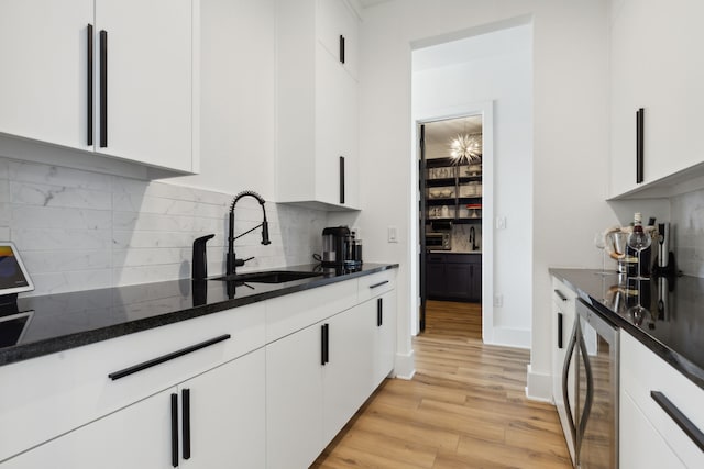 kitchen with white cabinetry, backsplash, sink, and light wood-type flooring