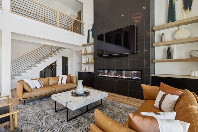 living room featuring a tiled fireplace, hardwood / wood-style floors, and a high ceiling