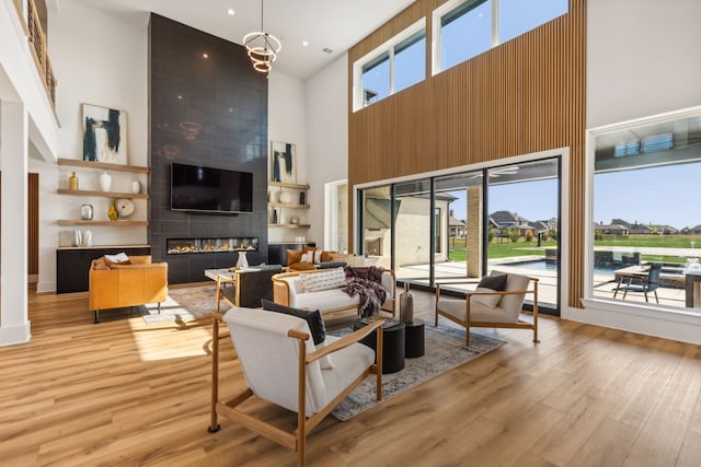 living room with an inviting chandelier, a towering ceiling, a fireplace, and light hardwood / wood-style floors