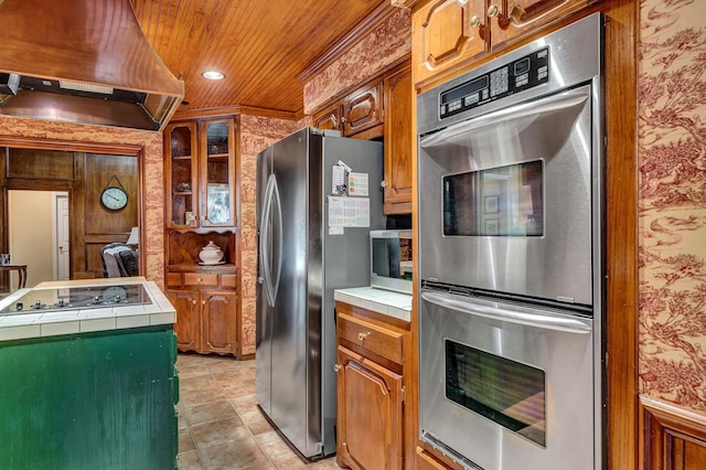 kitchen featuring brown cabinetry, tile countertops, wooden ceiling, stainless steel appliances, and extractor fan