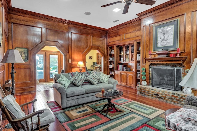 living room with built in features, wooden walls, a brick fireplace, and light hardwood / wood-style flooring